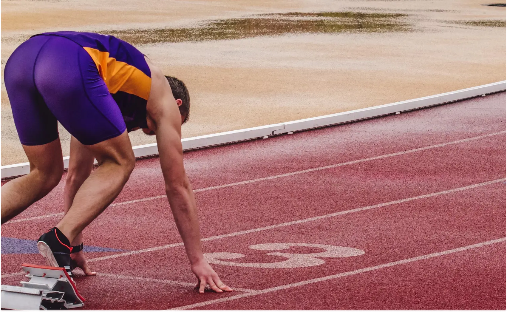 A male athlete leaning forward on a track, indicating preparation for a race